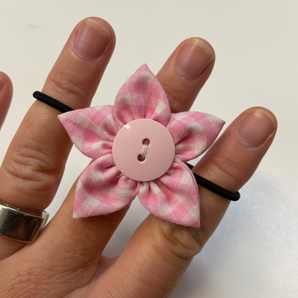 Pink flower-shaped hair clip with a button center on a person's finger against a white background