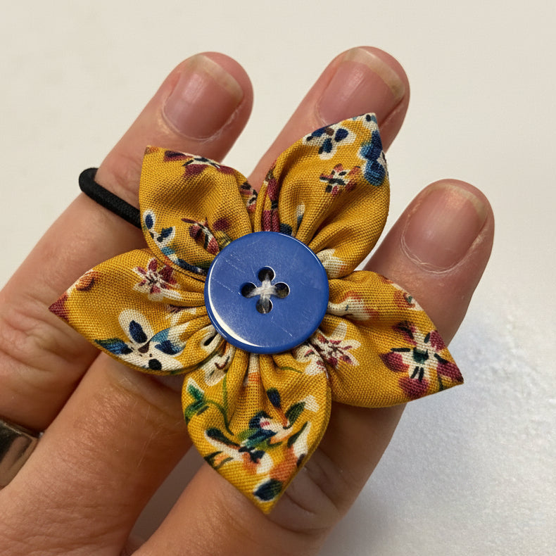 Hand holding a yellow fabric flower with a blue button in the center on a light background