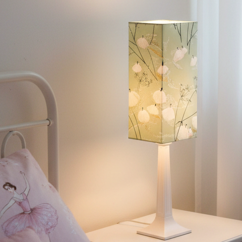 A modern table lamp with a rectangular light box featuring a sage green background and a pattern of white swans and black branches, mounted on a sleek white pedestal stand.