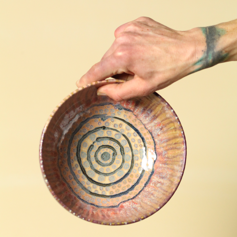 Hand holding a ceramic plate with concentric circle design on a beige background