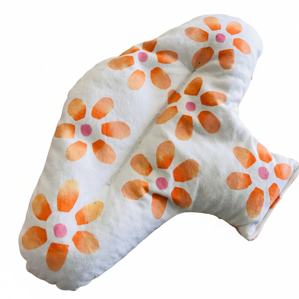 A white heat pack with a watercolor-style orange flower pattern and pink centers, resting on a light brown wooden surface.