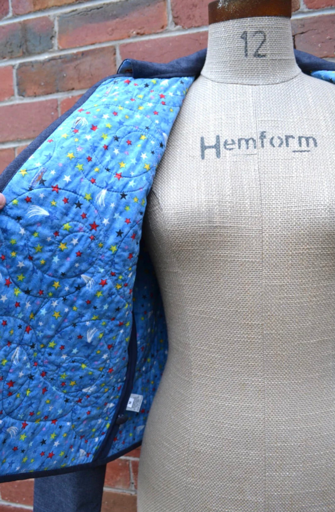 Mannequin wearing a quilted jacket showing the inside lining with colorful patterns against a brick wall.