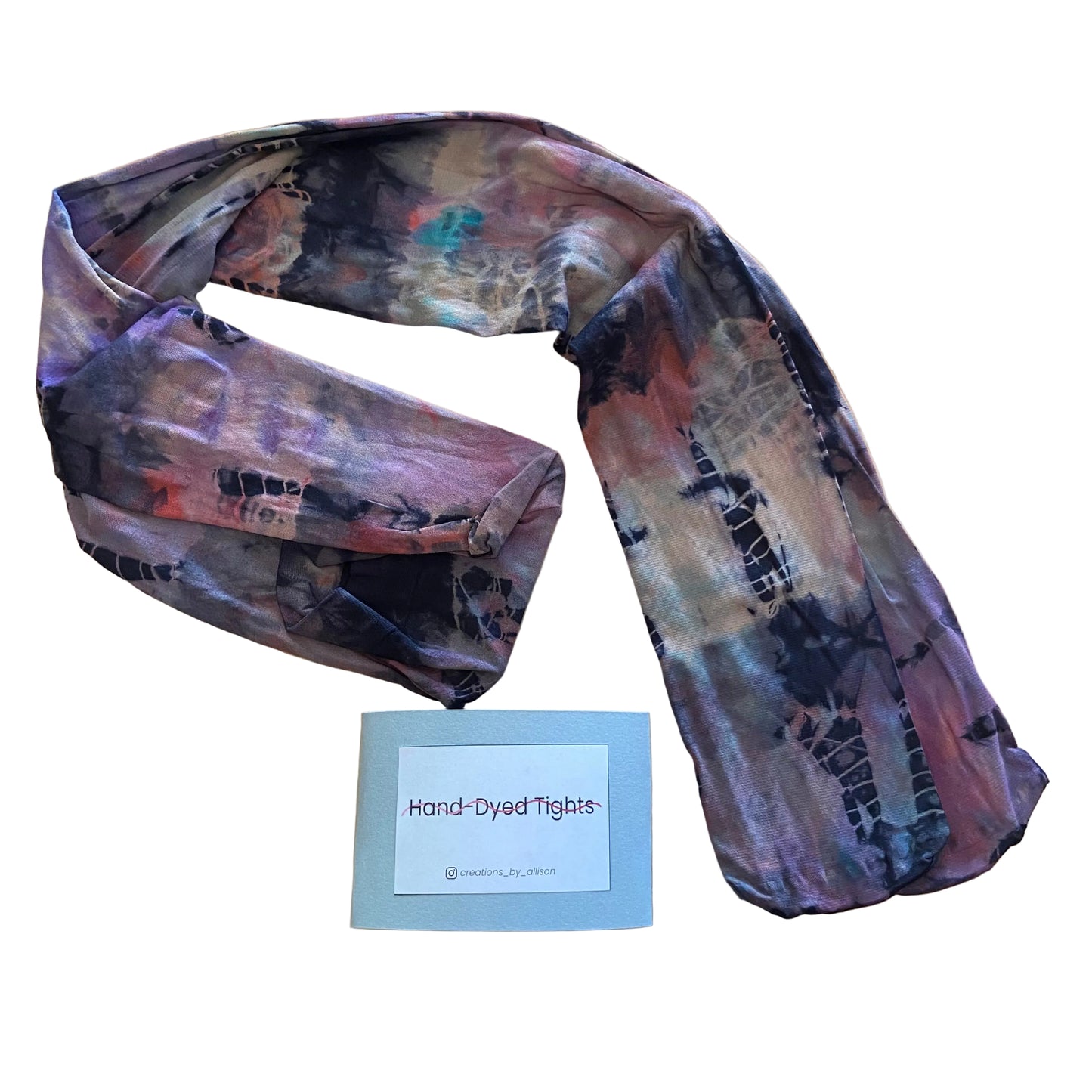 Hand-dyed tights with abstract pattern on a wooden surface, accompanied by a label.