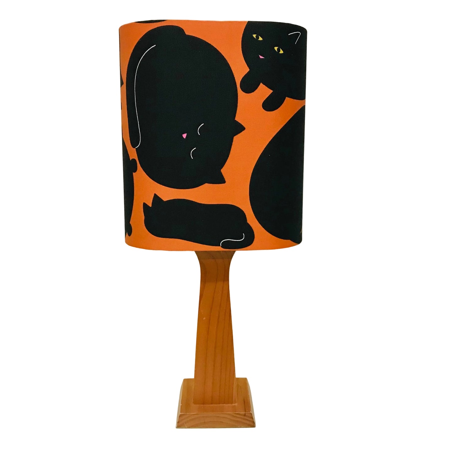 A table lamp with a cylindrical shade featuring a black cat pattern on an orange background, supported by a light brown wooden pedestal base.