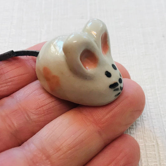 Small ceramic mouse figurine held in a hand against a white background