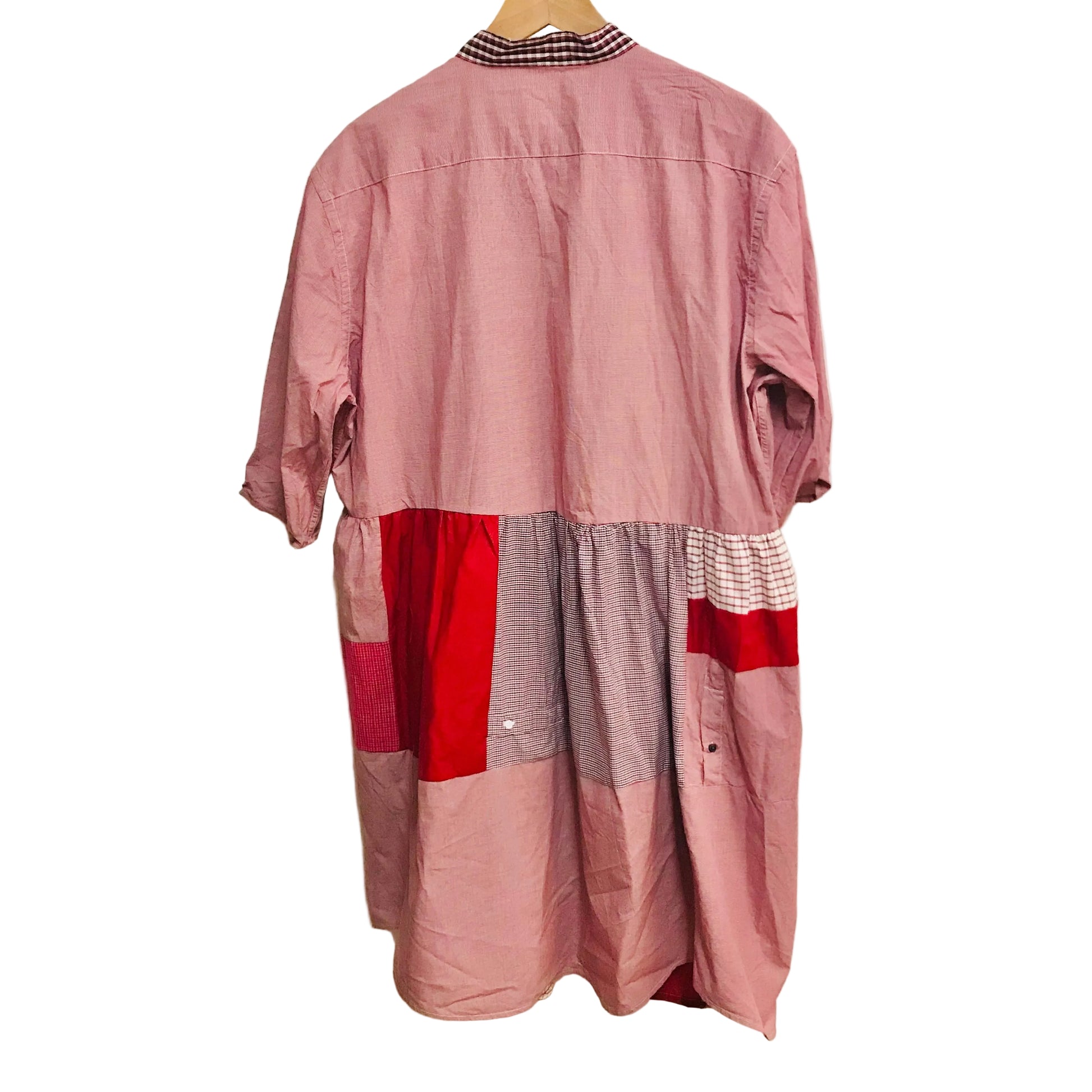 Patchwork dress with pink, red, and gray pattern on a hanger against a white wall.