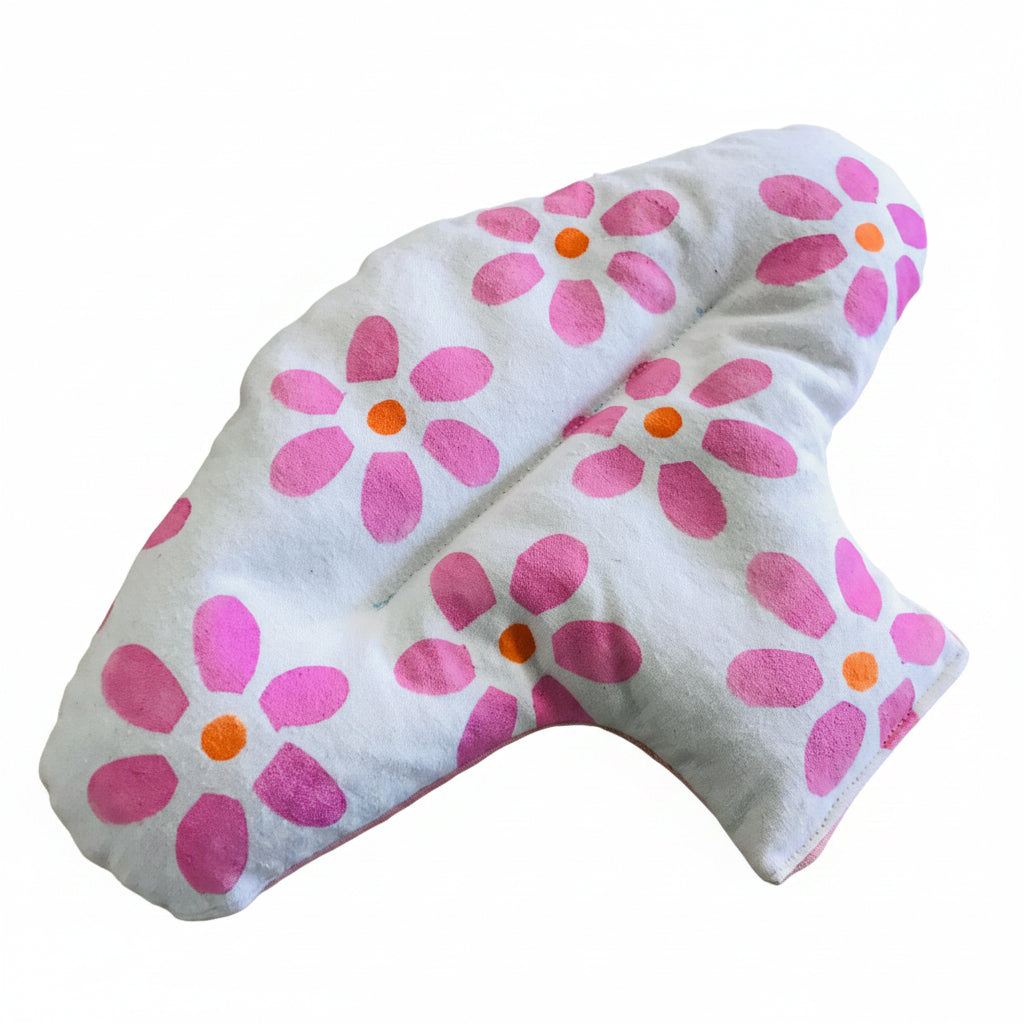 A white female lupin filled heat pack with a pink and orange floral pattern, laid flat on a light brown wooden surface.