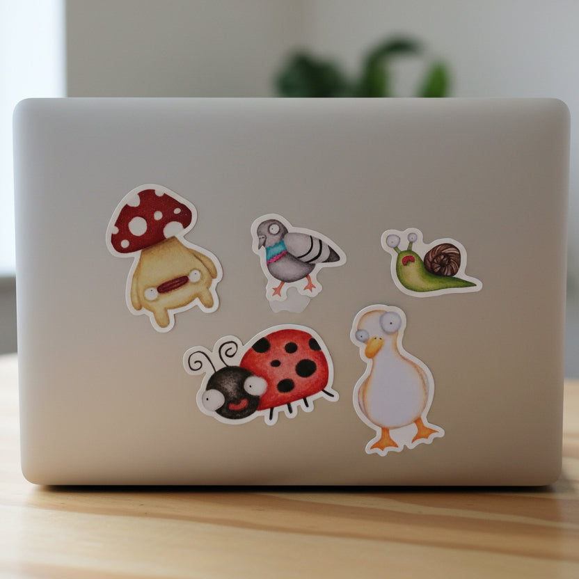 Five cute cartoon animal stickers arranged on a wooden tabletop. The stickers include a mushroom character with a red cap, a gray pigeon with a blue scarf, a green snail with a brown shell, a ladybug with a red and black shell, and a white duck with orange feet.
