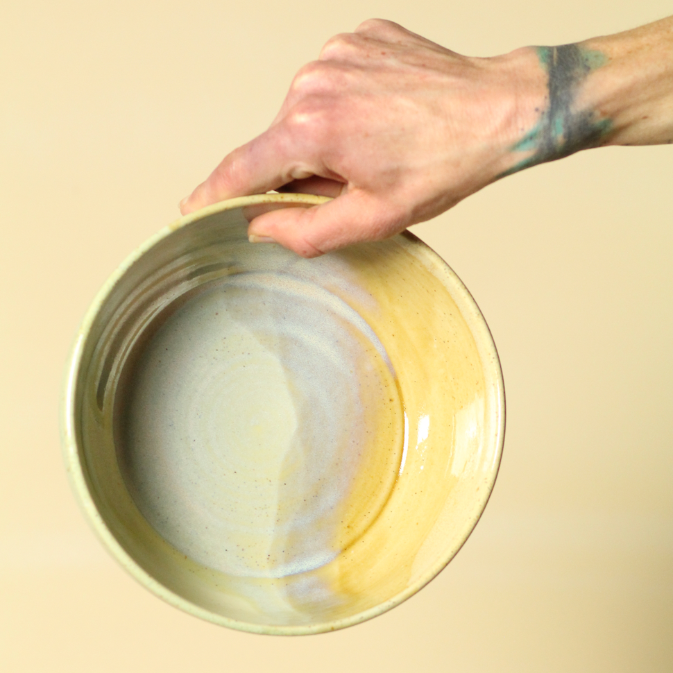 Hand holding a pottery bowl against a beige background