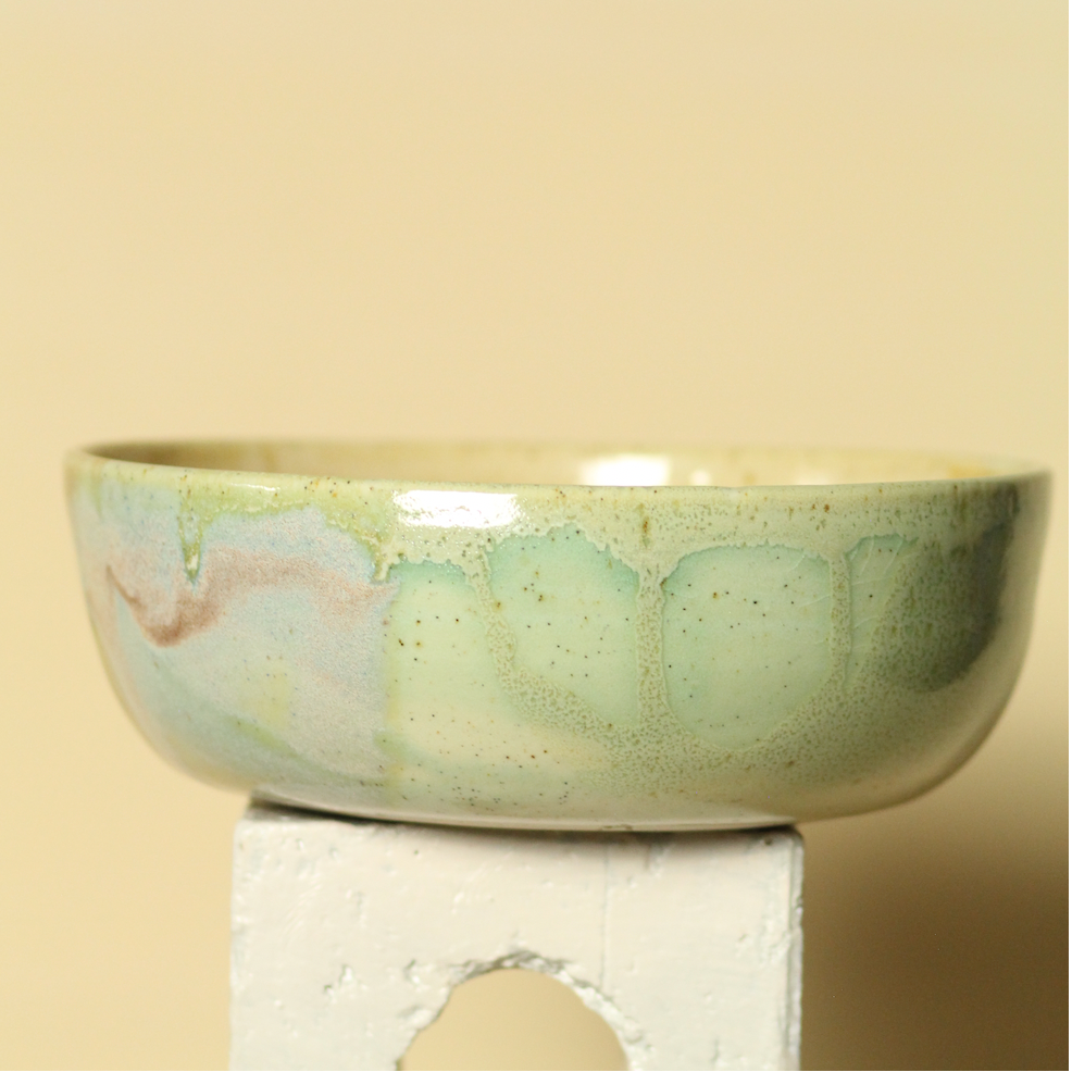 Ceramic bowl with green and beige glaze on a beige background
