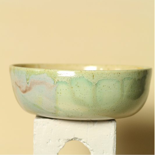 Ceramic bowl with green and beige glaze on a beige background
