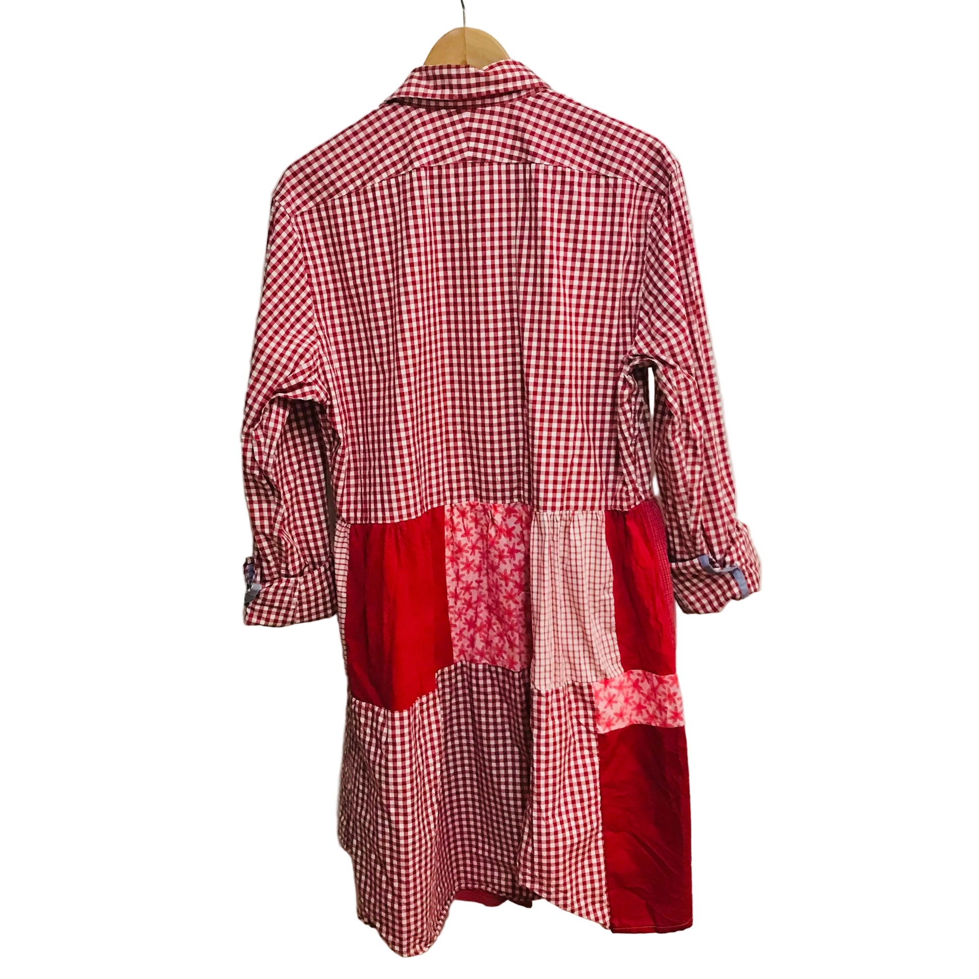 Red and white checkered dress with patchwork design on a hanger against a white wall.