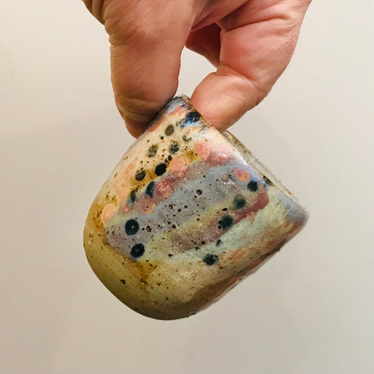 Hand holding a small ceramic cup with speckled glaze against a plain background