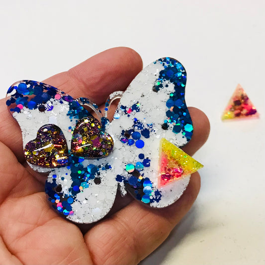 Butterfly-shaped earrings with glittery finish held in a hand on a white background