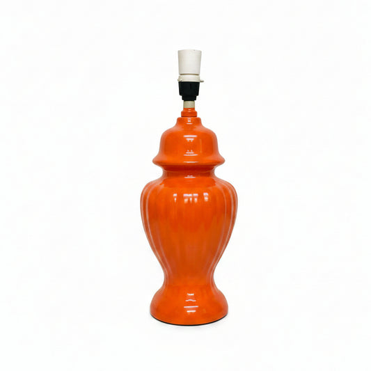 An orange ceramic table lamp with a ribbed vase-like body, a white and black socket, and a black power cord on a light gray background.