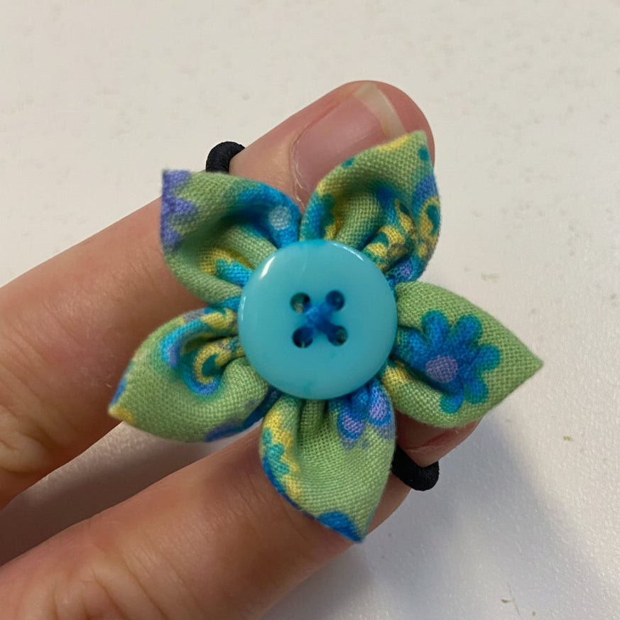 Hand holding a fabric flower hairtie with a button center against a white background