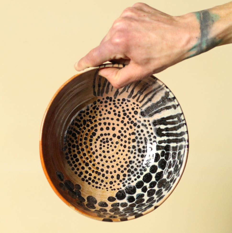 Hand holding a ceramic bowl with black dot pattern on a beige background