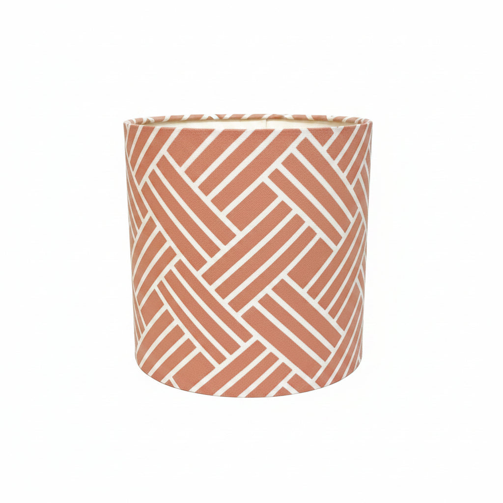 A cylindrical lampshade featuring a terracotta orange and white geometric herringbone pattern, set against a plain white background.
