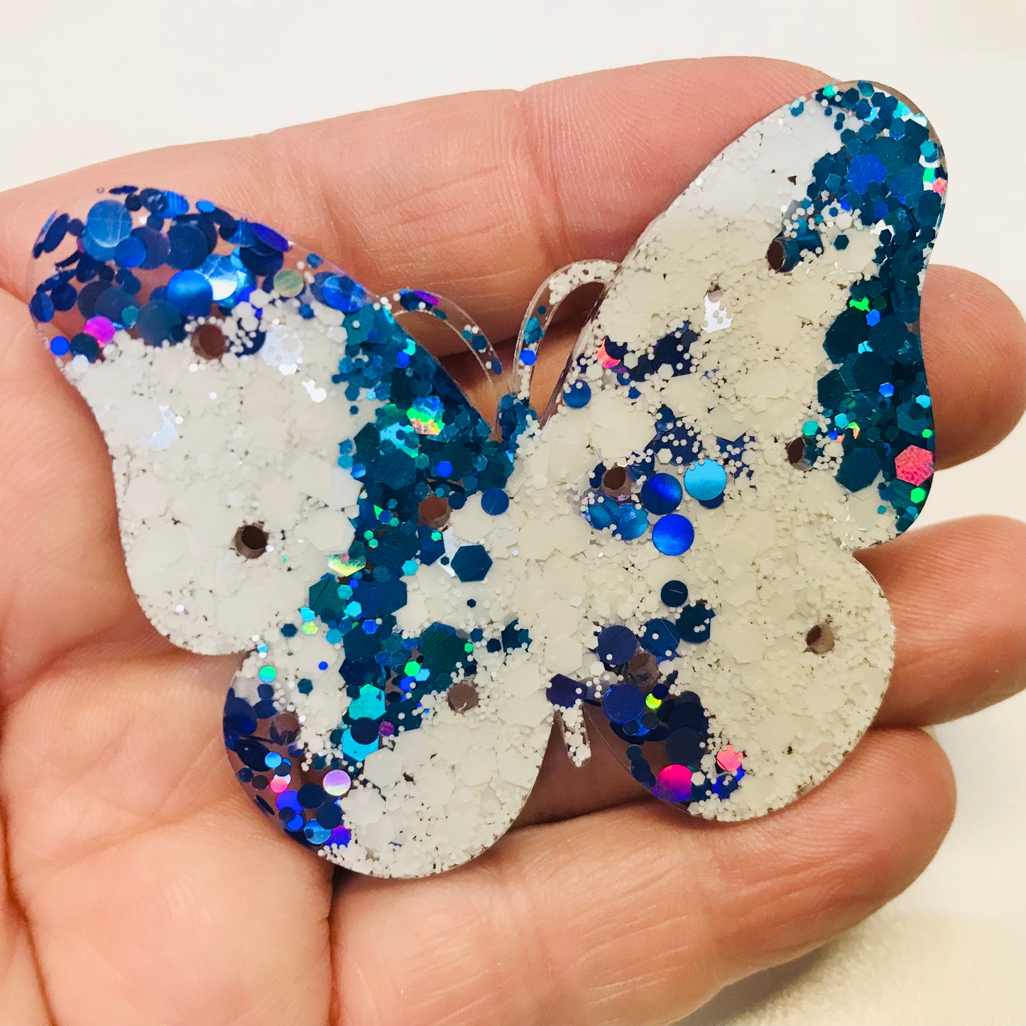 Butterfly-shaped object with blue and silver glitter held in a hand against a white background