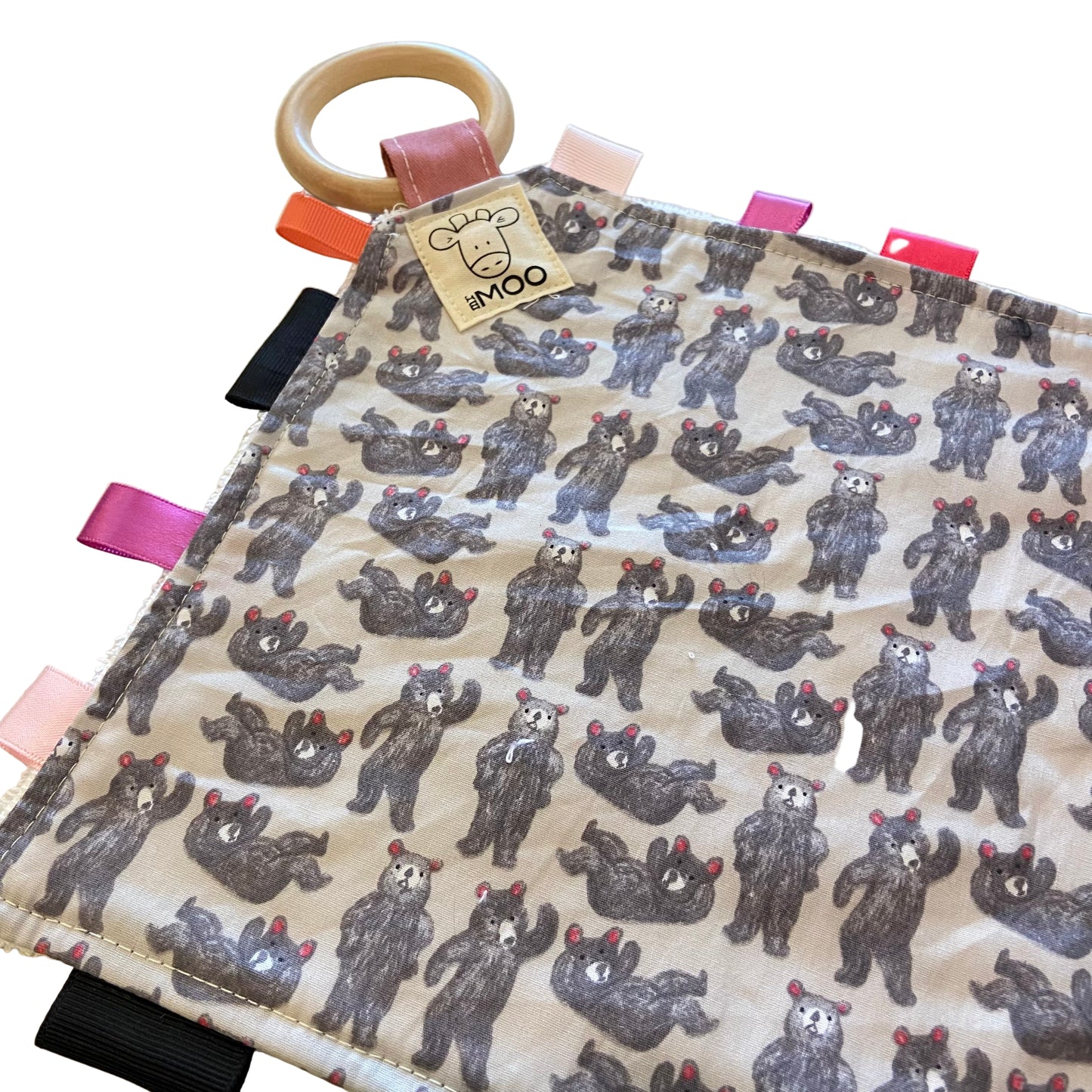 Fabric taggie teething toy with bear pattern and wooden ring on a beige background