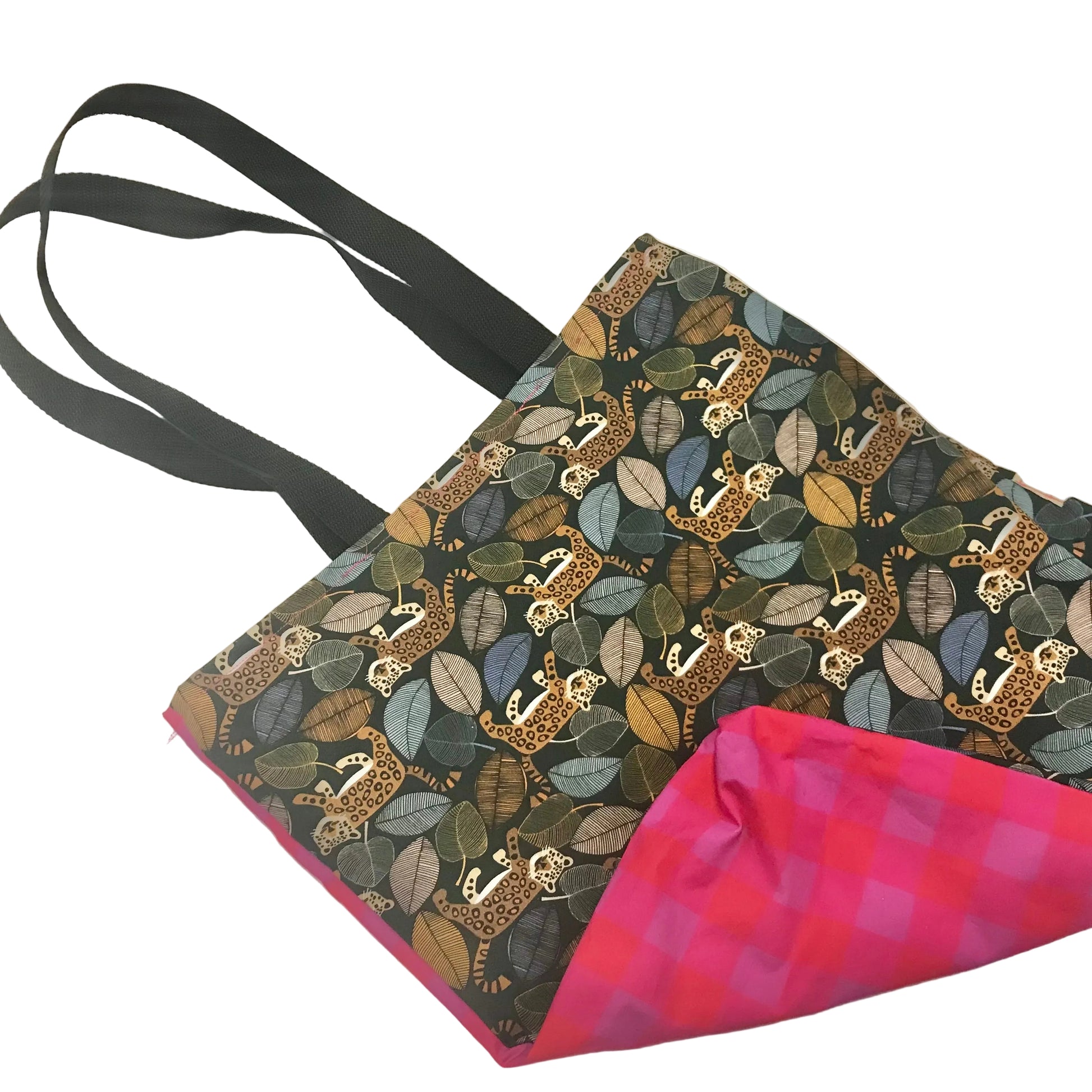 A fabric tote bag with black shoulder straps, featuring a dark patterned exterior with illustrated leopards and leaves in muted green, blue, and brown tones, and a bright pink and purple gingham lining visible at the corner.