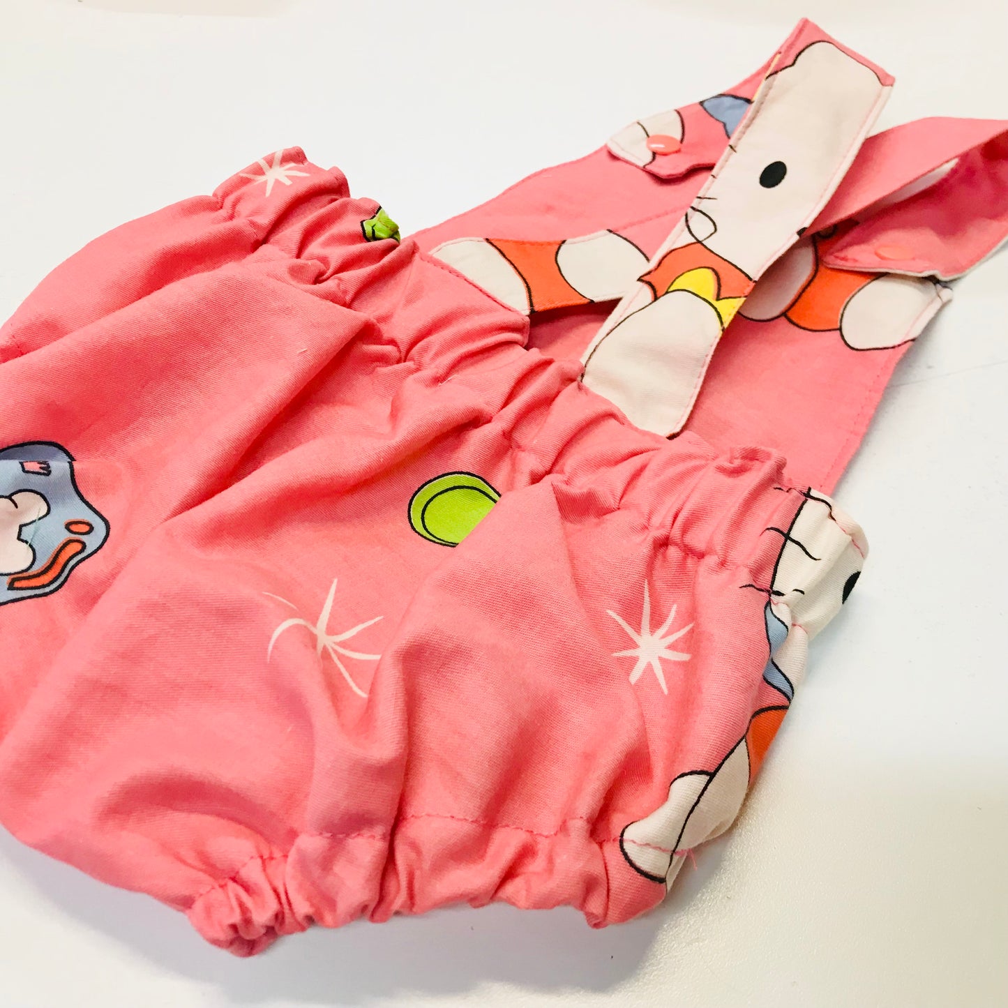 Pink baby romper with cartoon character on a white background, showing back with straps and elastic waistband