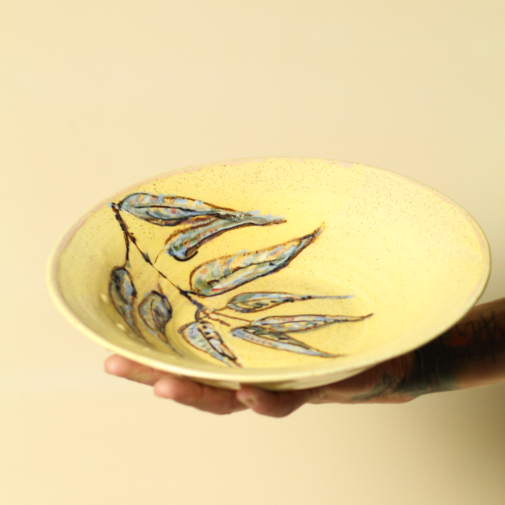 Ceramic plate with leaf design held by a hand against a beige background