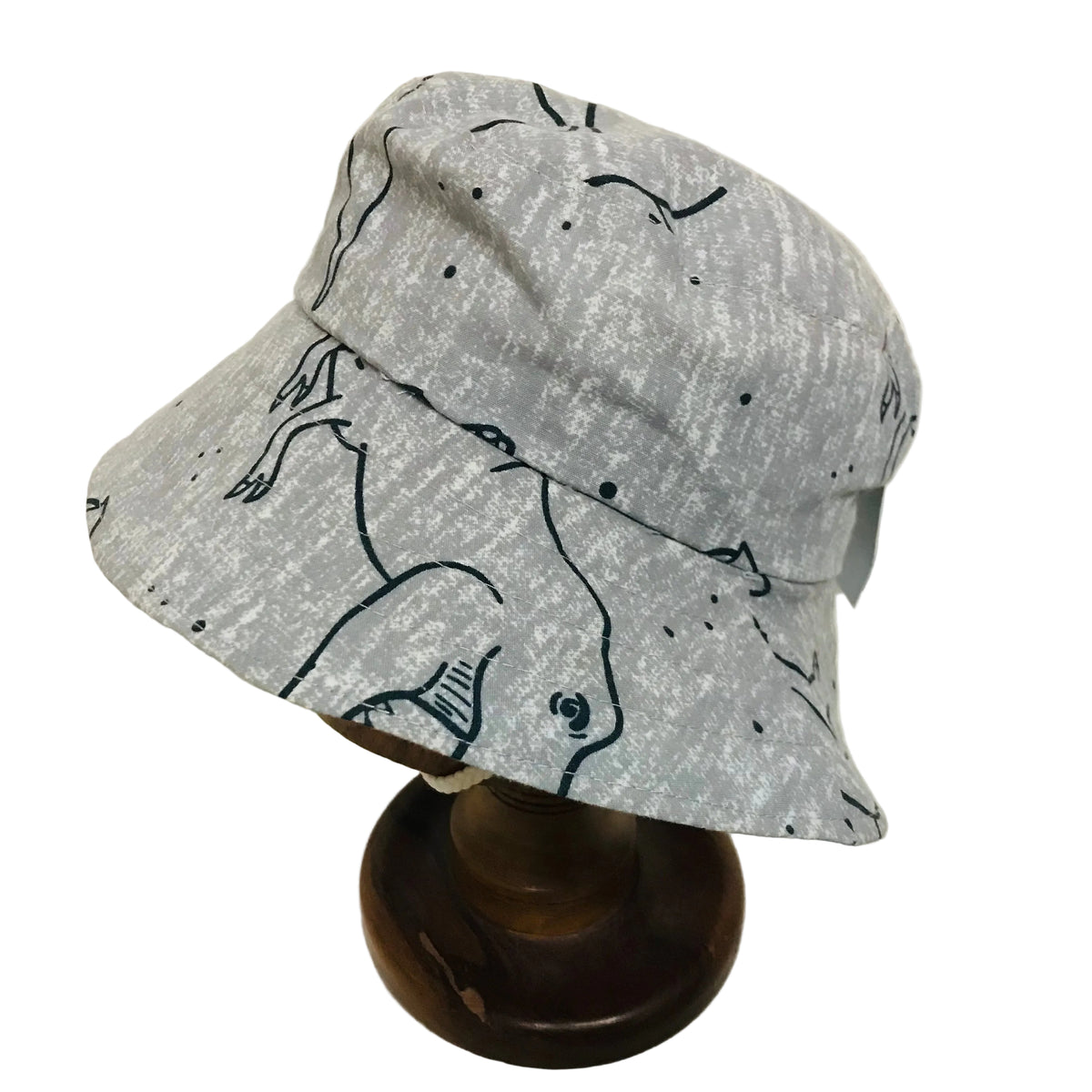 A light gray bucket hat with a black line-art print of a rabbit and small black dots, displayed on a wooden stand against a plain off-white background.