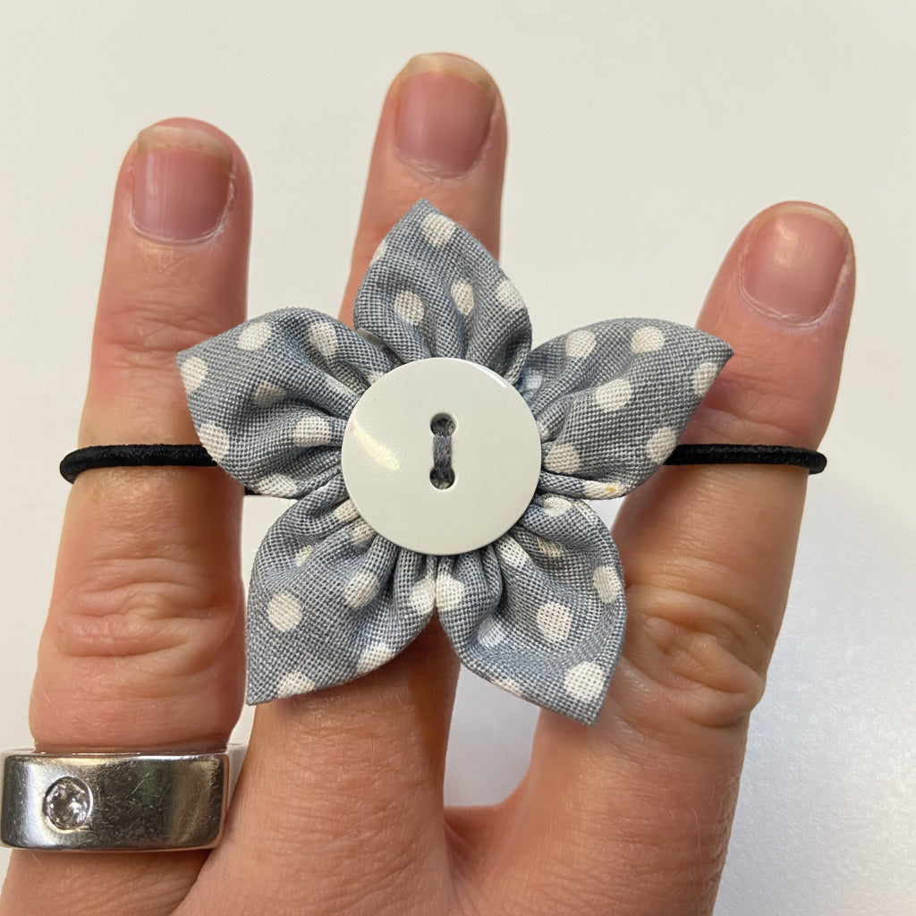 Gray polka dot bow hair clip with a button center held between fingers on a white background