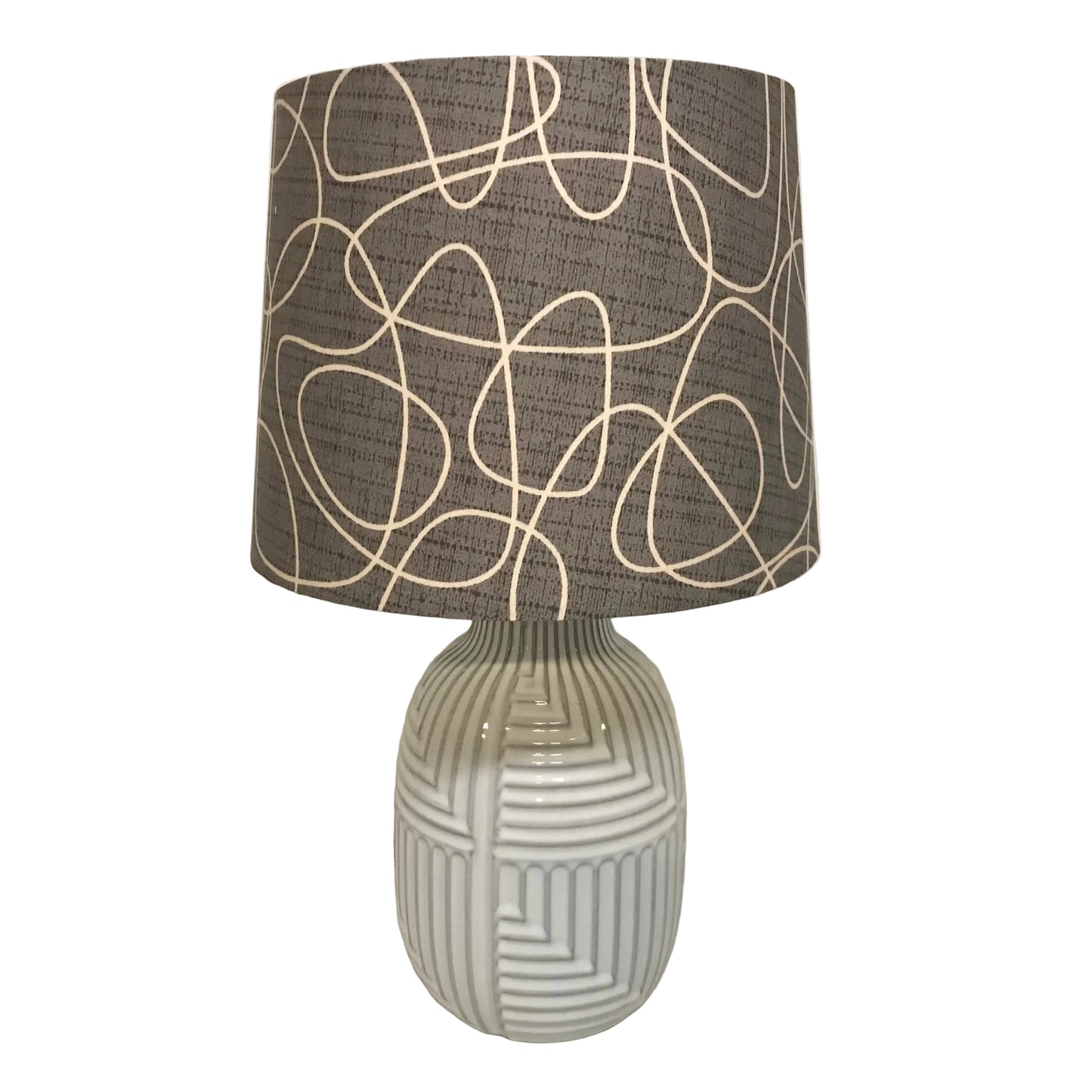 A table lamp with a textured dark gray drum shade featuring cream-colored abstract line patterns, mounted on a glossy white ribbed ceramic base.