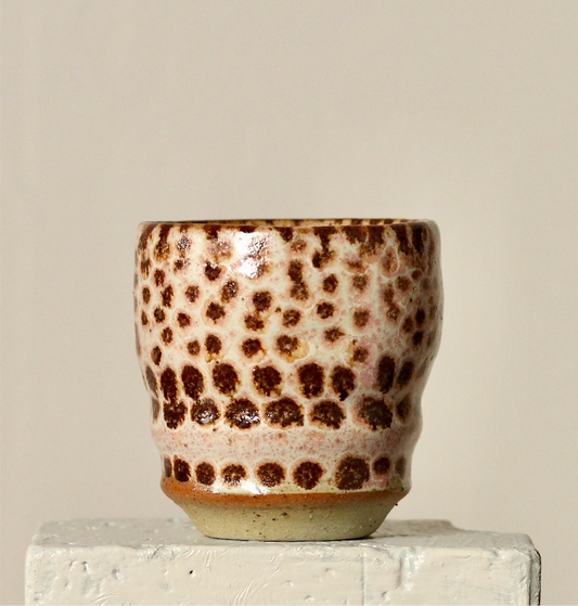 Ceramic espresso cup with brown dot pattern on a beige background
