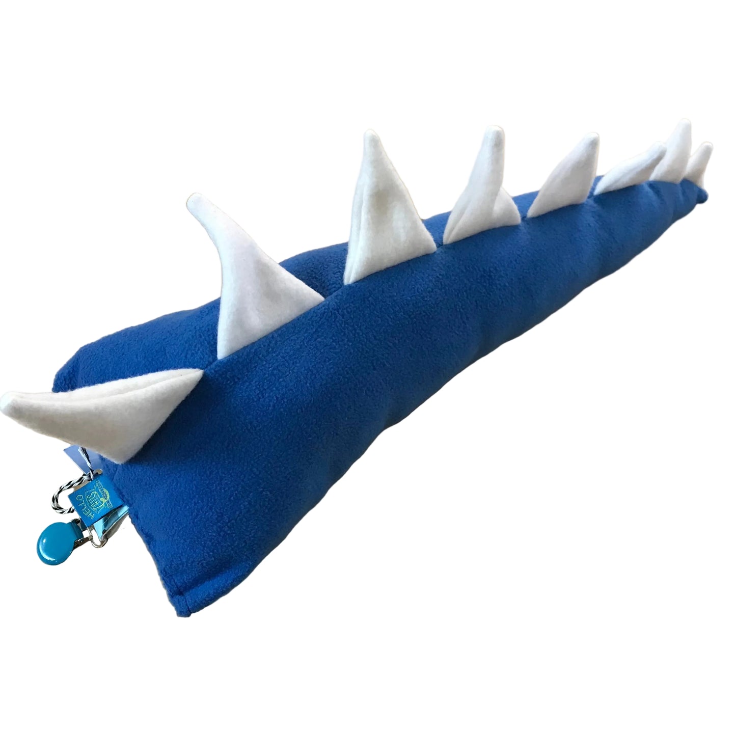 A blue felt dinosaur tail, featuring white felt spikes along the back and a small blue clip attached at the rear, placed on a light wood tabletop.