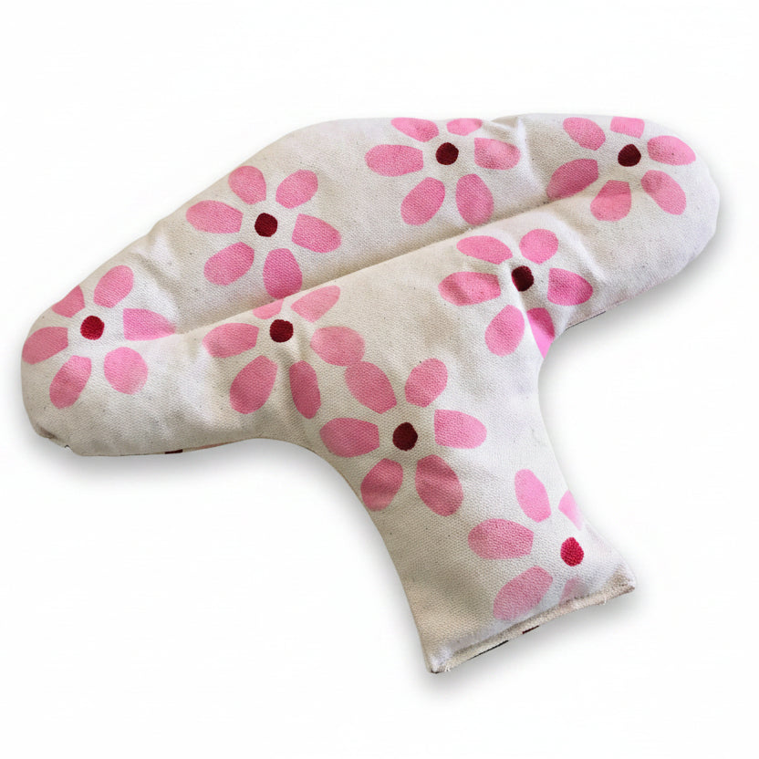 A fabric female menstrual relief heat pac with a pink floral pattern on a white background, resting on a light wood surface.