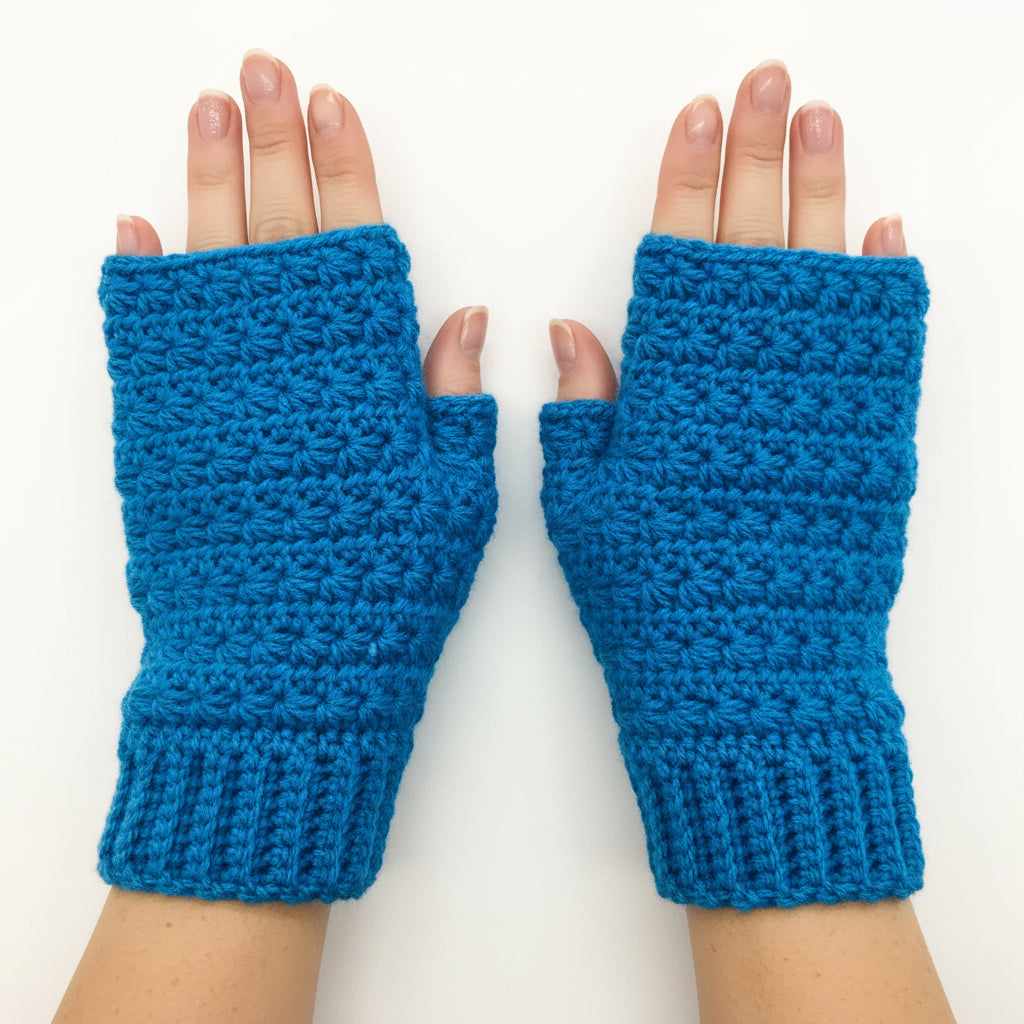 A pair of bright blue crocheted fingerless gloves or mittens laid flat on a light wood surface.