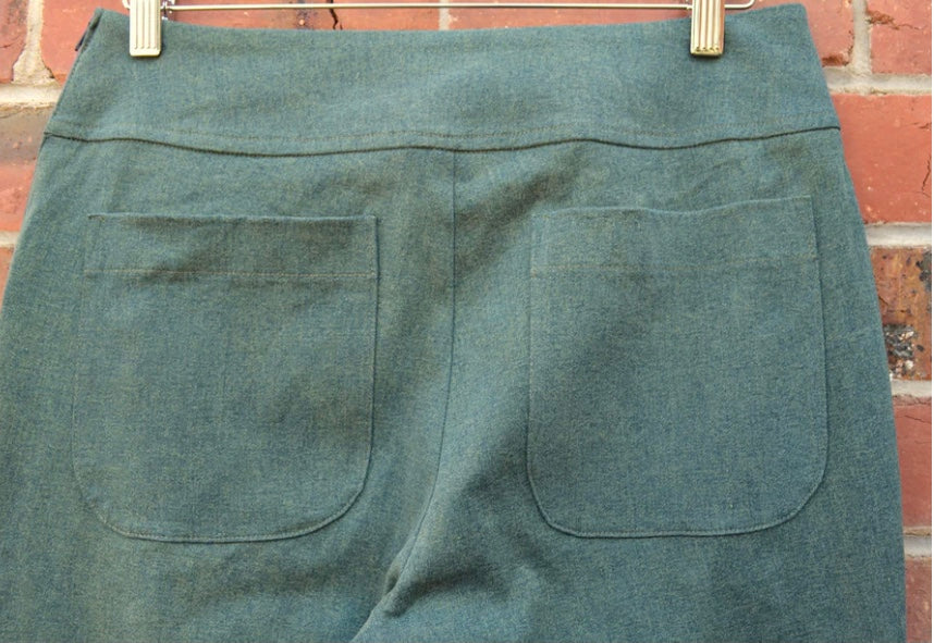 Green pants with two back pockets hanging against a brick wall.