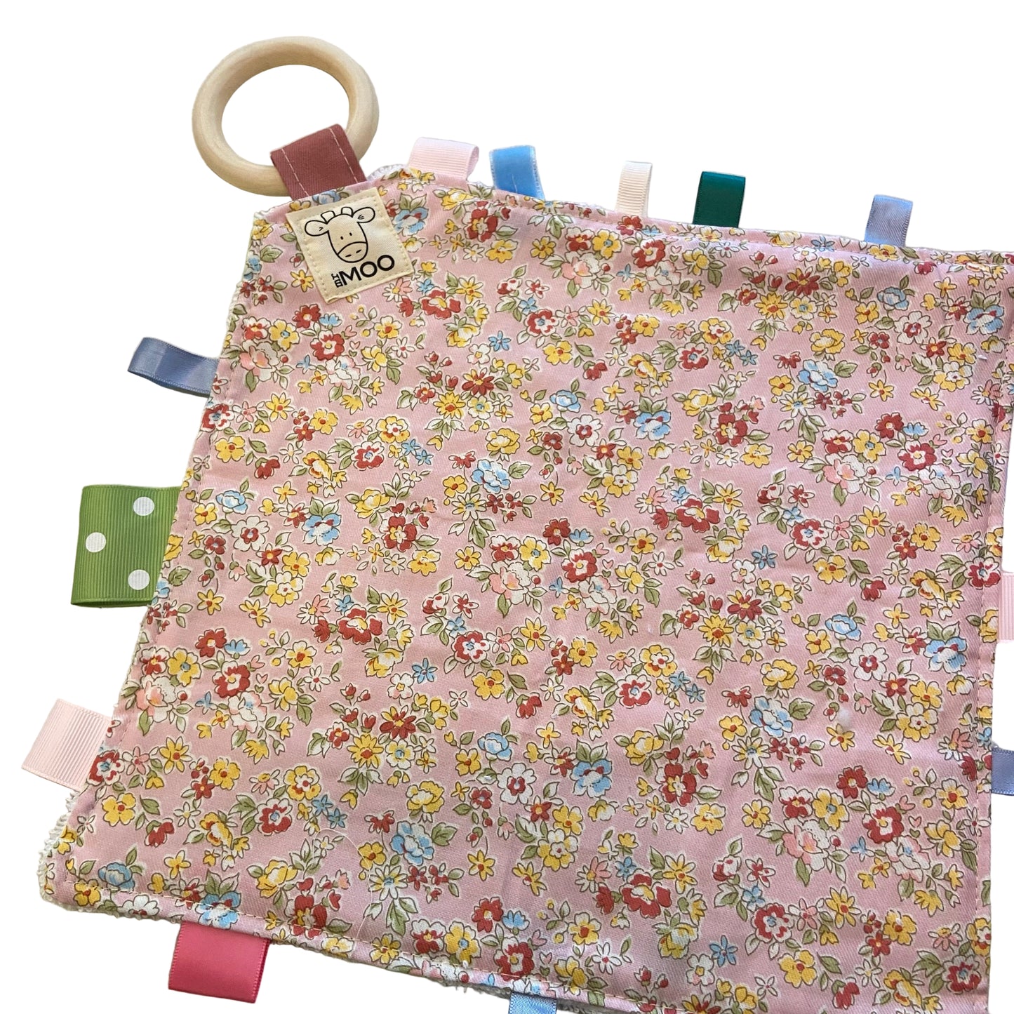 Floral fabric taggy blanket with wooden teething ring on a light background
