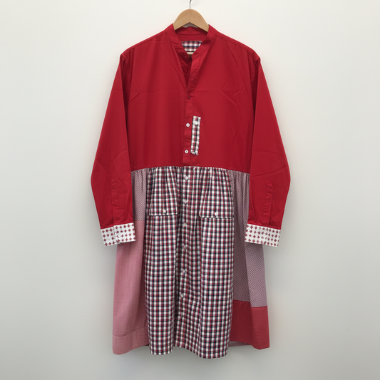A long-sleeve button-front dress or tunic with a color-blocked design, featuring a solid red upper section, a pink lower panel, and red-and-white gingham check fabric on the skirt and cuffs, hanging on a wooden hanger against a plain light gray wall.