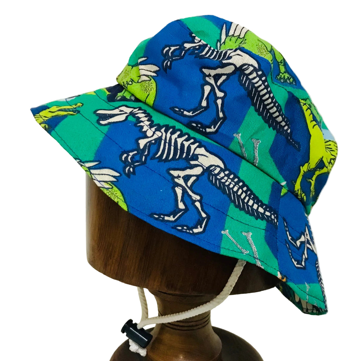 A bucket-style sun hat with a blue and green dinosaur skeleton print, displayed on a wooden mannequin head against a plain white background.
