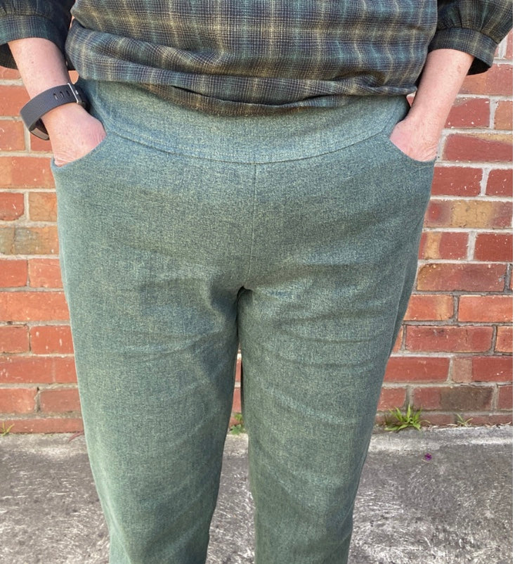 Person wearing green plaid pants and a checkered shirt against a brick wall.