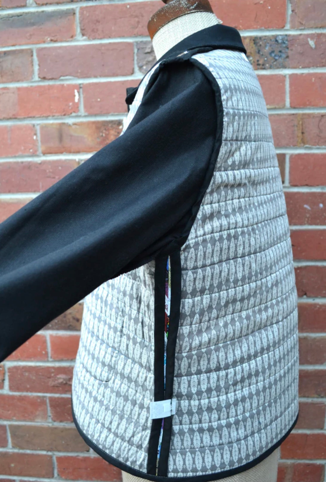 Mannequin wearing a quilted jacket inside out to show lining with black accents against a brick wall.