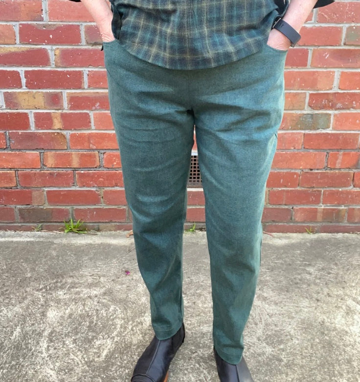 Person wearing green pants and a plaid shirt against a brick wall.