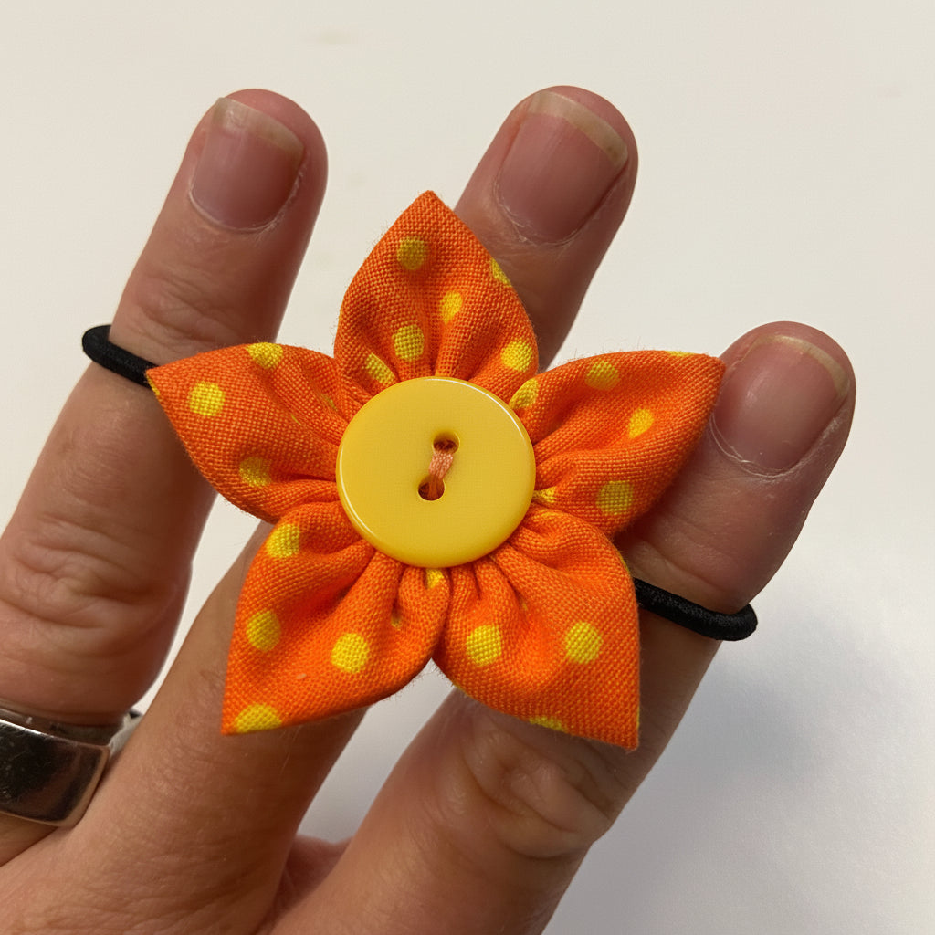 Orange flower-shaped hair clip with yellow polka dots and a yellow button center held between fingers.