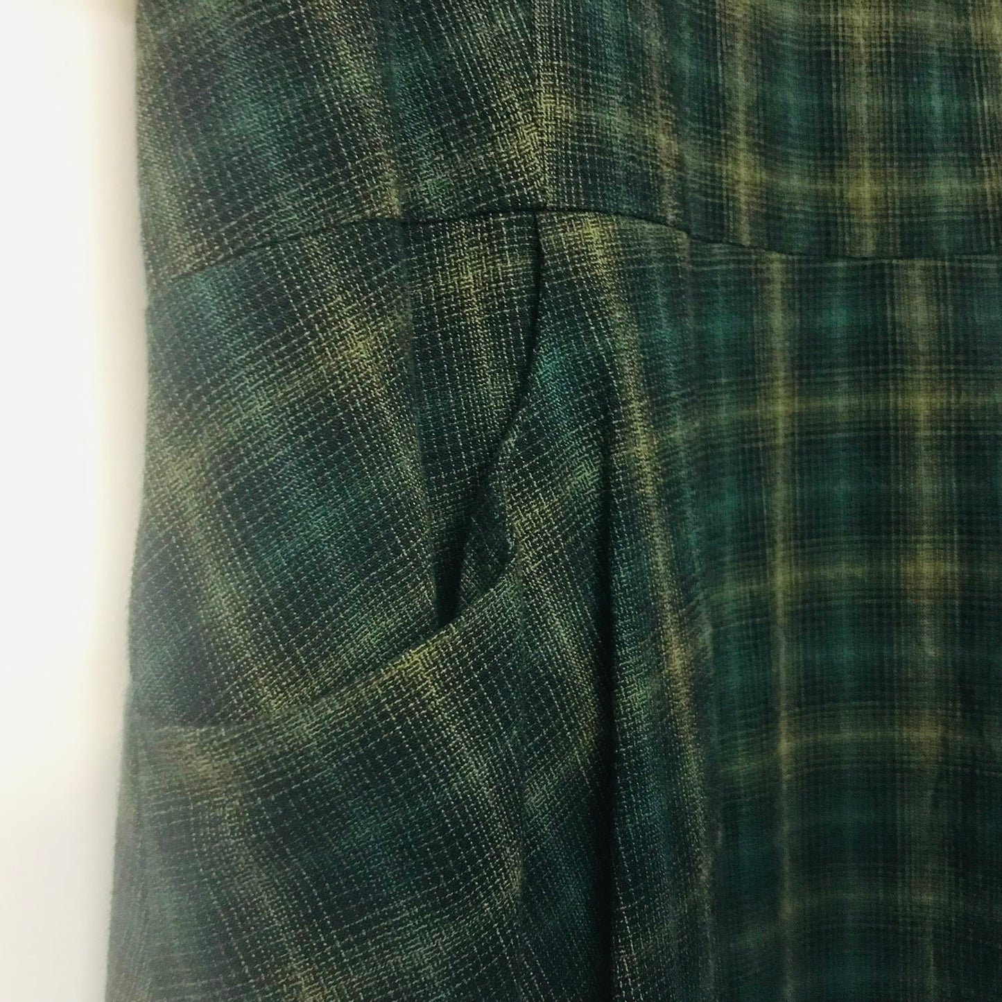 Close-up of a dark green and black plaid fabric garment, showing a side pocket and pleated texture.