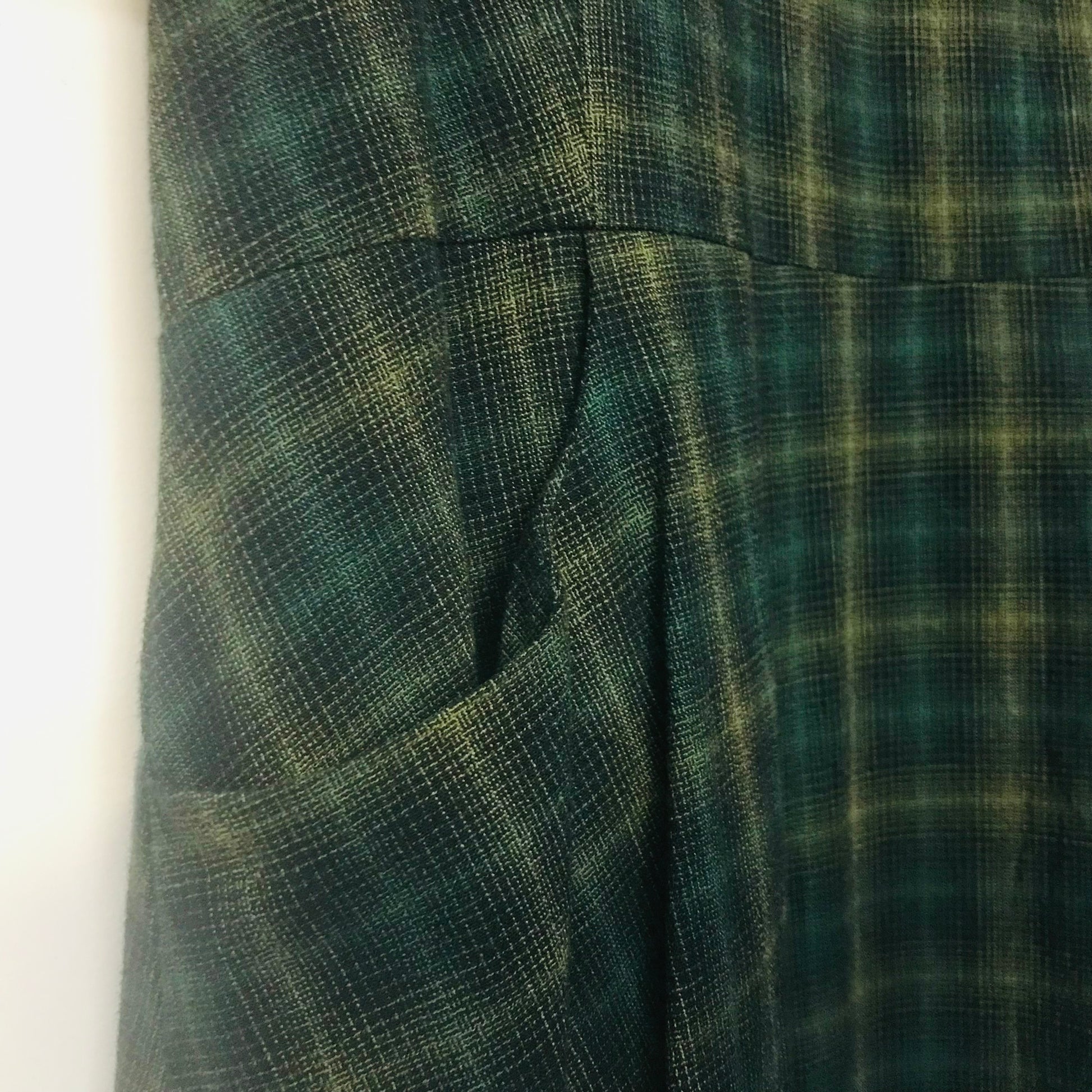 Close-up of a dark green and black plaid fabric garment, showing a side pocket and pleated texture.