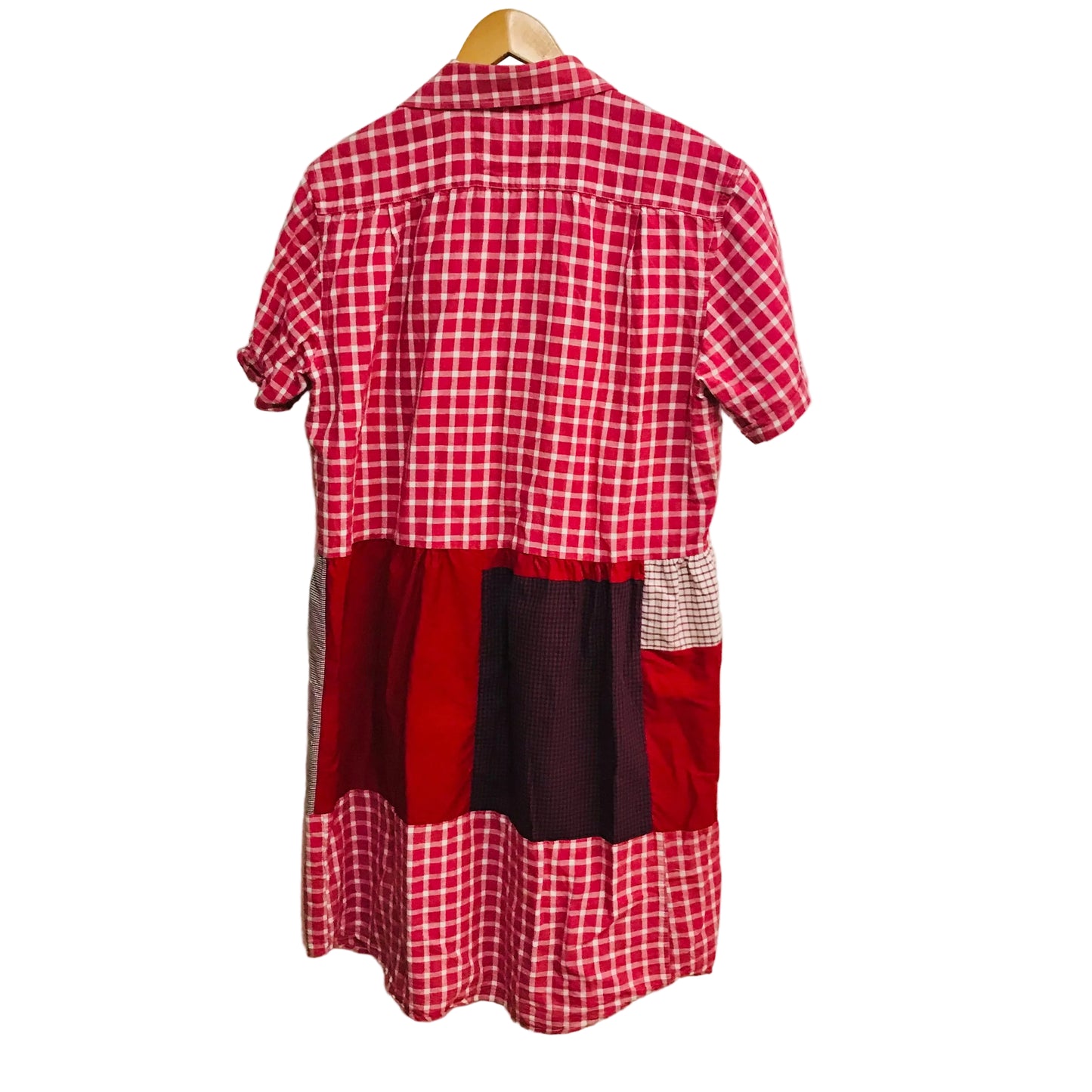 Red and white checkered dress with patchwork design on a hanger against a white wall.