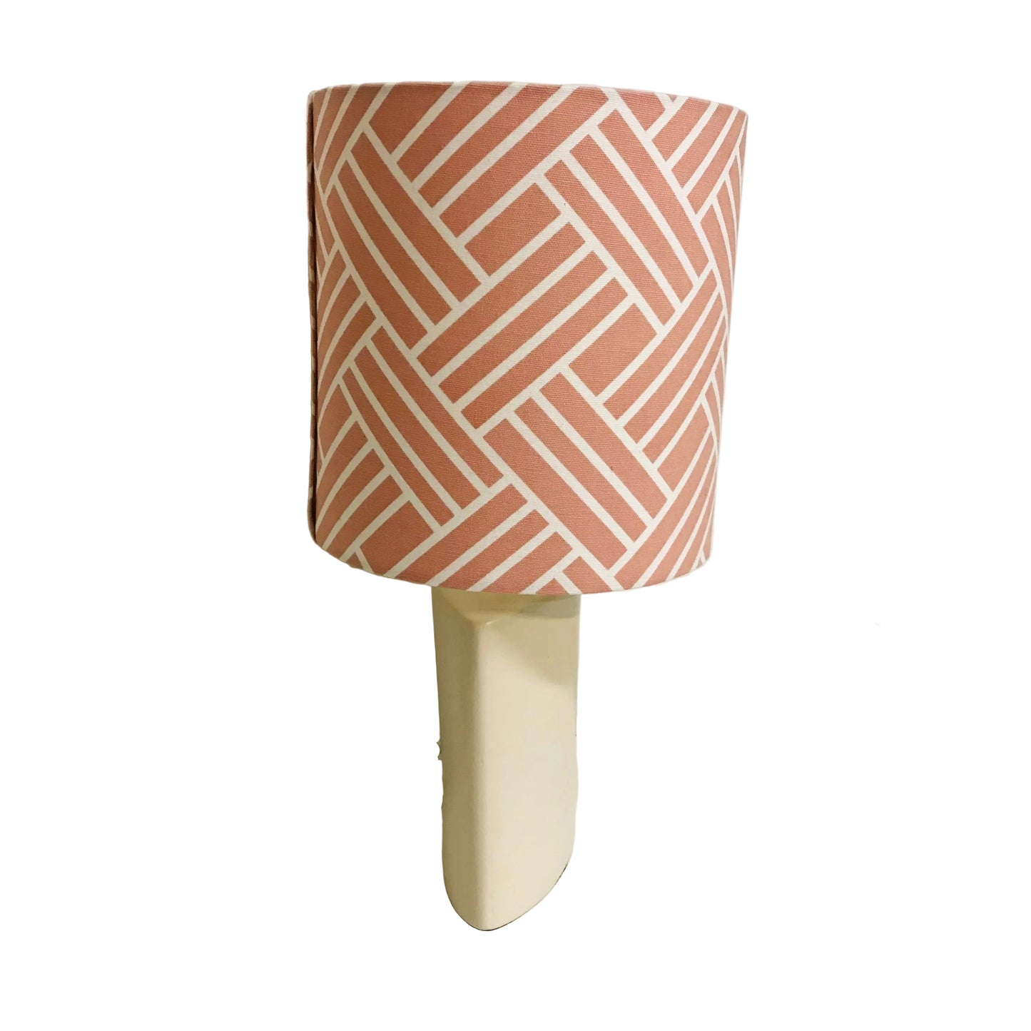 A table lamp with a cylindrical drum shade featuring a terracotta pink and white geometric herringbone pattern, mounted on a solid cream-colored rectangular base.