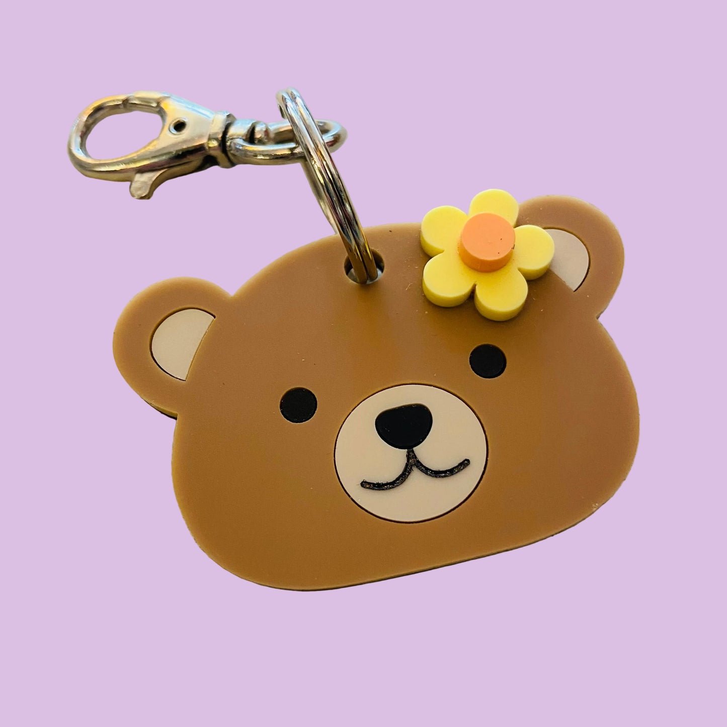 Brown bear-shaped keychain with a flower on a beige surface