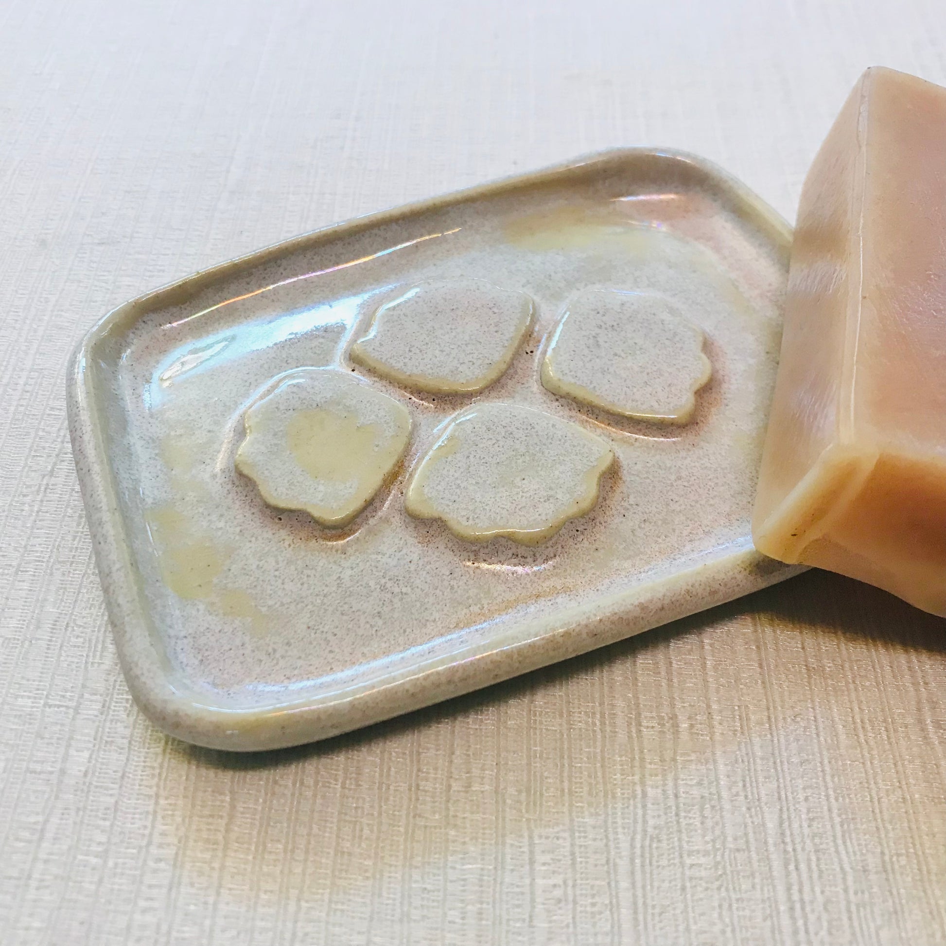 Bar of soap on a ceramic soap dish with raised petals on a light background