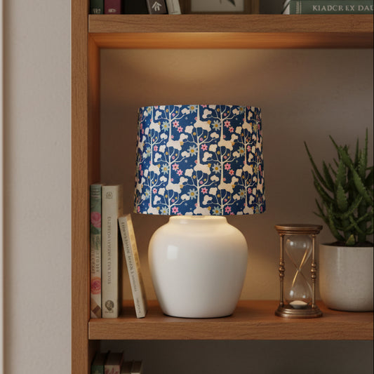 Lamp with a blue floral patterned shade on a white base on a bookshelf
