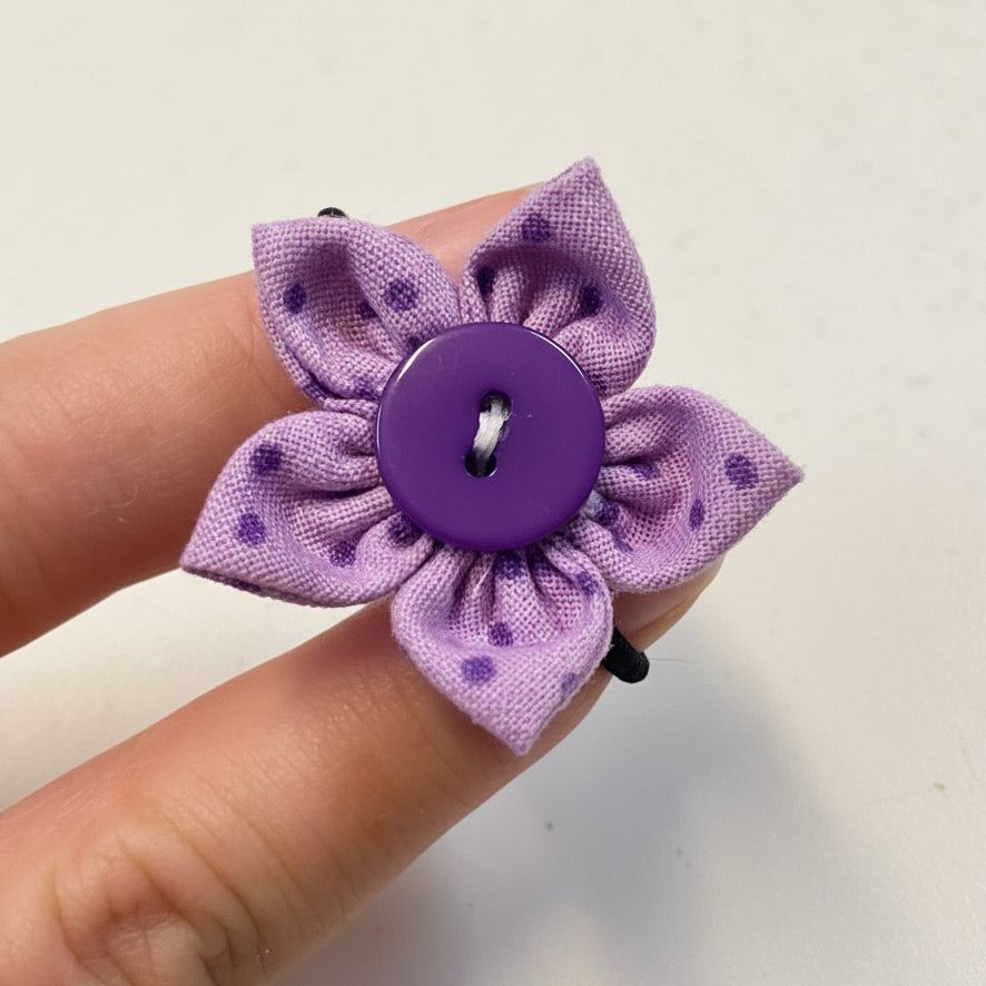 Purple flower-shaped hair clip with a button center held between fingers on a light background